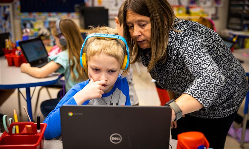 A teacher helps a student on a Chromebook